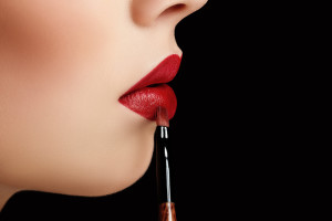 closeup macro photo of brush with lipstick and natural great red lips of young woman on black background